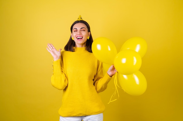 Mulher jovem e bonita em um suéter amarelo com balões comemora um feriado de aniversário, pulando de felicidade