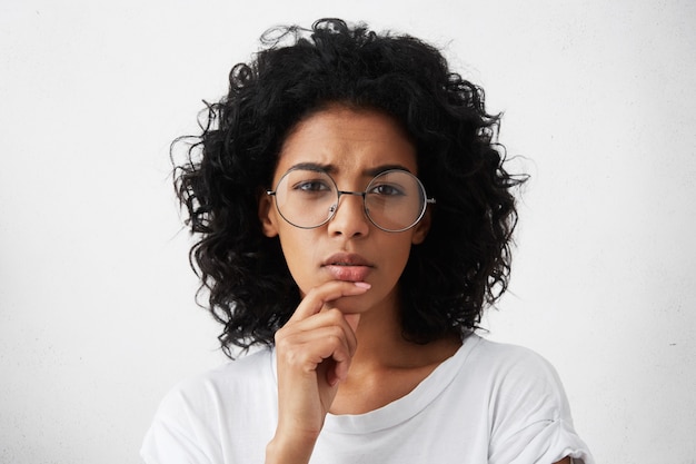 Mulher jovem e bonita em uma camiseta branca e grandes óculos redondos apertando os olhos