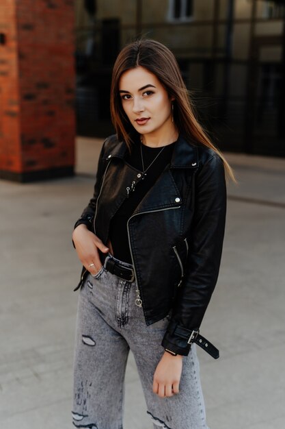 Mulher jovem e bonita em uma jaqueta de couro preta posando na rua