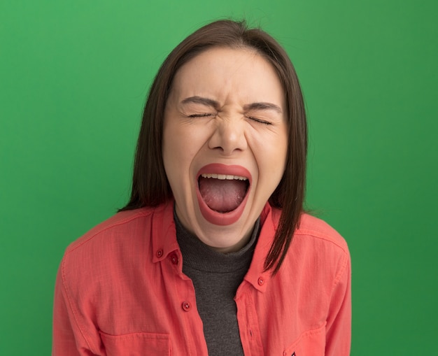 Foto grátis mulher jovem e bonita estressada gritando com os olhos fechados, isolada na parede verde