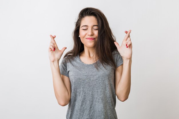 Mulher jovem e bonita fazendo um desejo cruzou os dedos, sorte, olhos fechados, gesto de esperança,