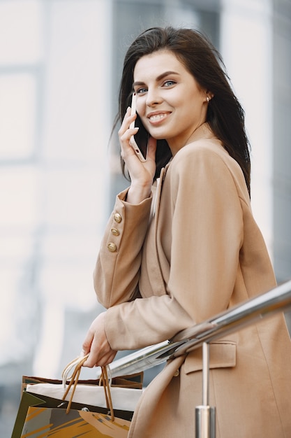 Mulher jovem e bonita feliz com sacolas de compras, falando em um telefone celular de um shopping center