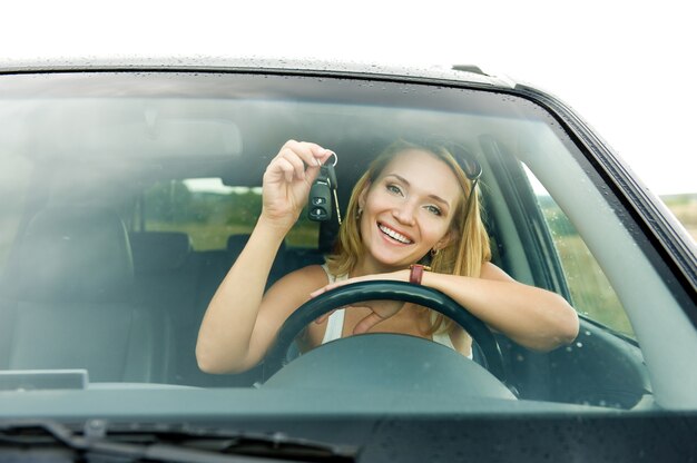 Mulher jovem e bonita feliz no novo carro com as chaves - ao ar livre