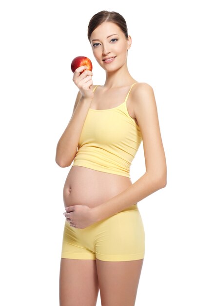 Mulher jovem e bonita grávida com uma bela barriga segurando uma maçã vermelha isolada no branco