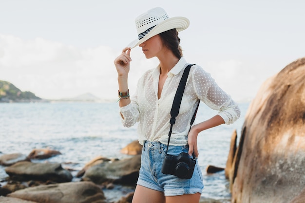 Mulher jovem e bonita hippie nas férias de verão na Ásia, relaxando em uma praia tropical, câmera fotográfica digital, estilo boho casual, paisagem do mar, corpo magro bronzeado, viajar sozinho