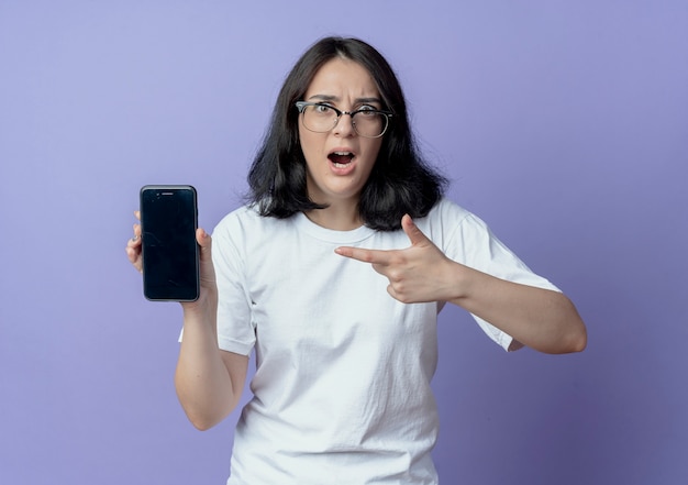 Mulher jovem e bonita impressionada de óculos mostrando e apontando para o celular