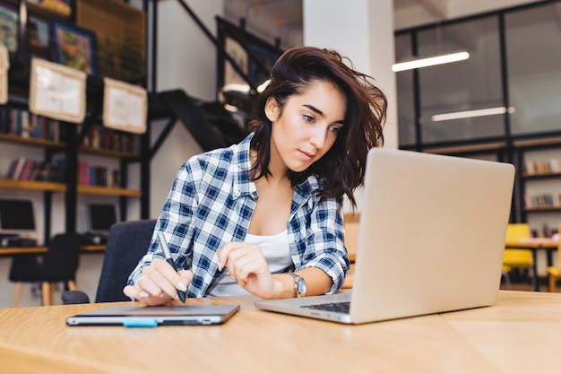 Mulher jovem e bonita inteligente trabalhando com o laptop na mesa na biblioteca. Estudando na universidade, aprendendo, freelancer, trabalhando, pesquisando na internet, estudante inteligente, trabalhador.