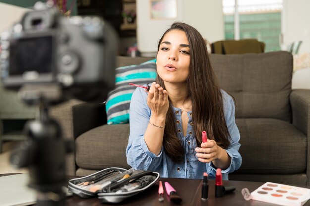 Mulher jovem e bonita mandando um beijo para uma câmera enquanto gravava um blog de vídeo sobre beleza e maquiagem