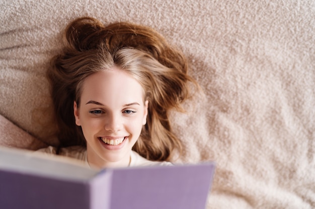 Mulher jovem e bonita na cama em casa curtindo o livro favorito