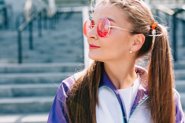 Mulher jovem e bonita na moda com roupas elegantes, óculos cor de rosa e sorrindo