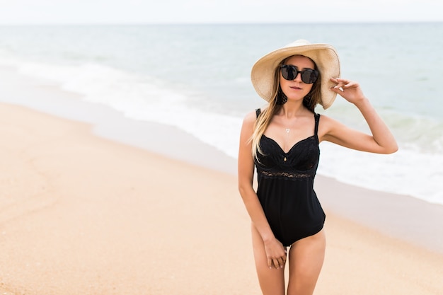 Mulher jovem e bonita nas férias de verão usando chapéu de palha e biquíni de praia, apreciando a vista para o mar