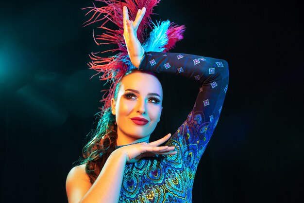 Mulher jovem e bonita no carnaval e fantasia de baile de máscaras com luzes de néon coloridas na parede preta
