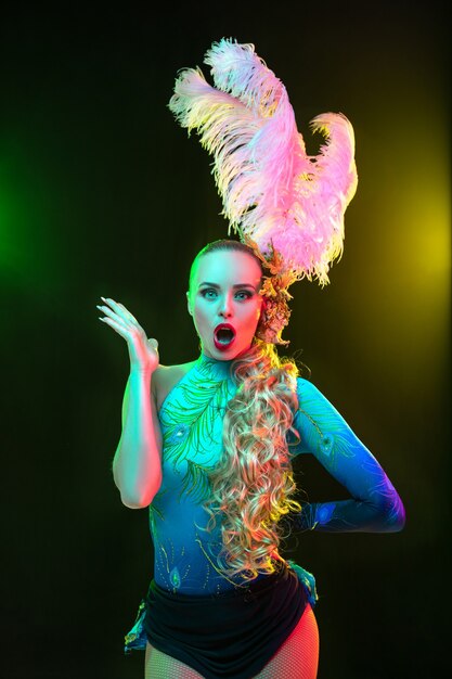 Mulher jovem e bonita no carnaval e fantasia de baile de máscaras com luzes de néon coloridas