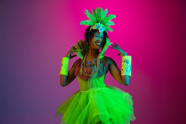 Mulher jovem e bonita no carnaval, elegante traje de máscaras com penas dançando no fundo gradiente em neon.