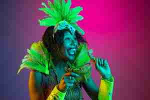 Foto grátis mulher jovem e bonita no carnaval, elegante traje de máscaras com penas dançando no fundo gradiente em neon.