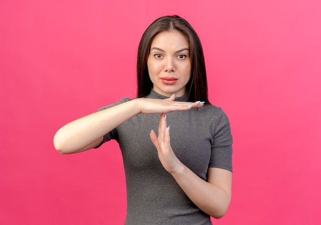 Mulher jovem e bonita olhando para a câmera e gesticulando para o tempo limite isolado em um fundo rosa com espaço de cópia