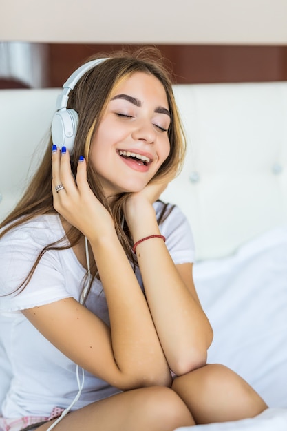 Mulher jovem e bonita ouvindo música em fones de ouvido na cama