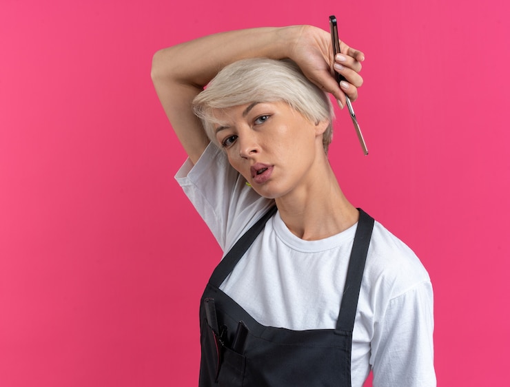 Foto grátis mulher jovem e bonita satisfeita de uniforme segurando uma navalha isolada na parede rosa