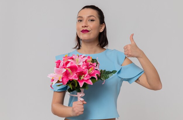 Mulher jovem e bonita satisfeita segurando um buquê de flores e apontando para cima