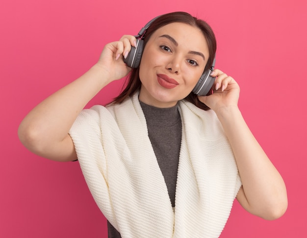 Mulher jovem e bonita satisfeita usando e agarrando fones de ouvido