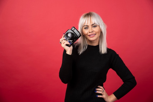 Foto grátis mulher jovem e bonita segurando uma câmera em pé contra um fundo vermelho. foto de alta qualidade