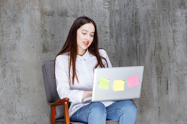 Mulher jovem e bonita sentada na poltrona trabalhando no laptop. Foto de alta qualidade