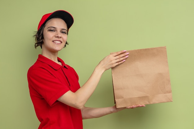 Mulher jovem e bonita sorridente, entregadora, segurando uma embalagem de papel para comida