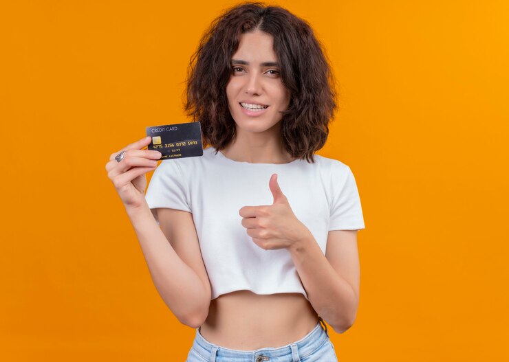 Foto grátis mulher jovem e bonita sorridente segurando o cartão e mostrando o polegar na parede laranja isolada com espaço de cópia