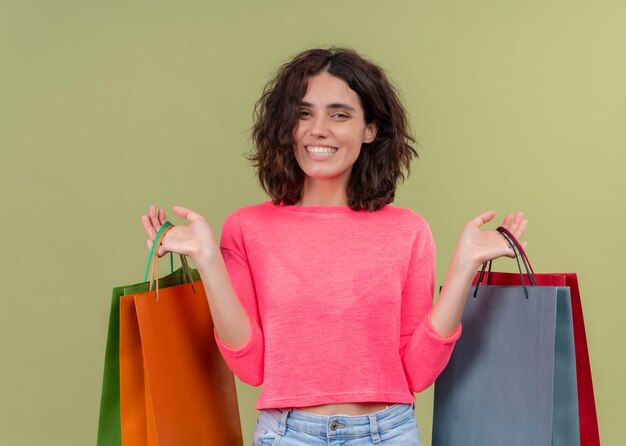 Mulher jovem e bonita sorridente segurando sacolas de papelão na parede verde isolada