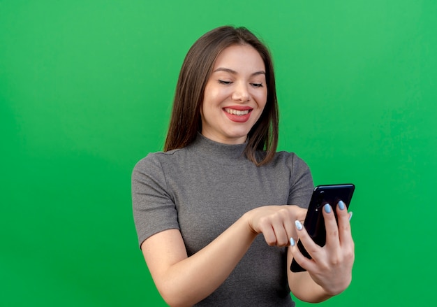 Mulher jovem e bonita sorridente usando telefone celular isolado em um fundo verde com espaço de cópia