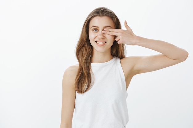 Mulher jovem e bonita sorrindo e cobrindo os olhos com dois dedos