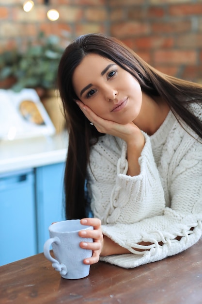 Mulher jovem e bonita tomando café ou chá na cozinha