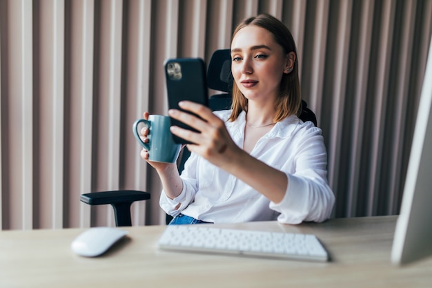 Mulher jovem e bonita trabalhando online com um pc e um telefone em uma área de trabalho no escritório