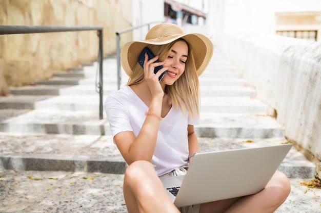 Mulher jovem e bonita vestindo roupa casual de verão sentada na escada da rua