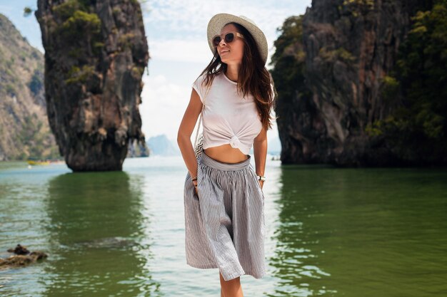 Mulher jovem e bonita viajando na Tailândia, férias de verão, estilo casual, óculos de sol, chapéu, saia de algodão, camiseta, sorridente, feliz, aventuras