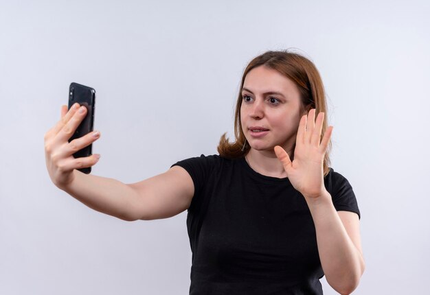 Mulher jovem e casual satisfeita segurando um telefone celular e gesticulando para o telefone em um espaço em branco isolado