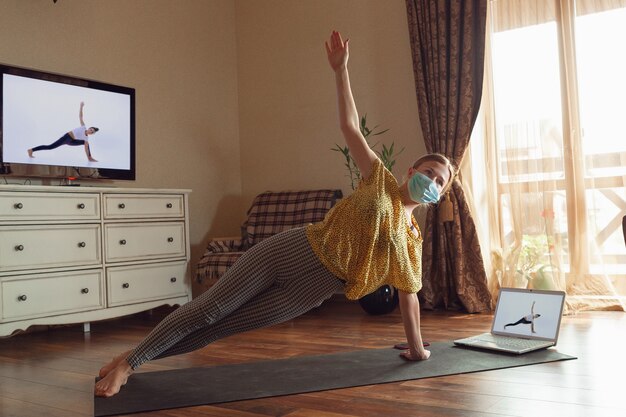 Mulher jovem e desportiva fazendo aulas de ioga online e praticando em casa enquanto está em quarentena.