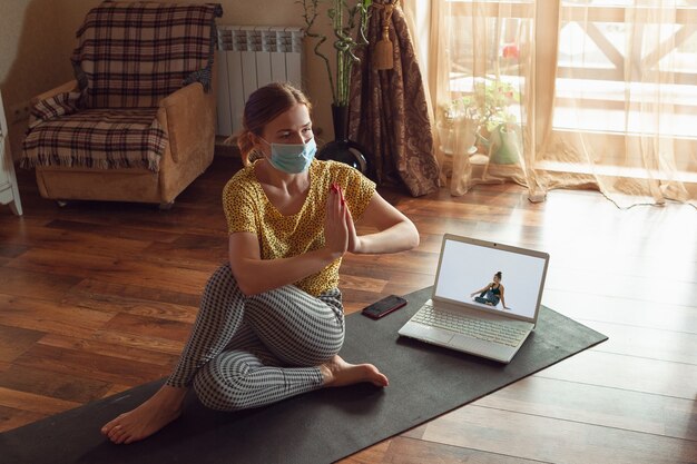 Mulher jovem e desportiva fazendo aulas de ioga online e praticando em casa enquanto está em quarentena.