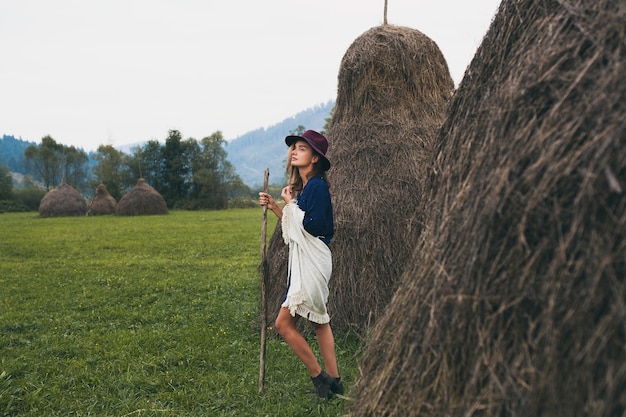 Mulher jovem e elegante caminhando no campo na paisagem de montanhas e campos verdes com roupa de outono