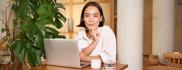 Mulher jovem e elegante confiante com laptop sentado no café e trabalhando como freelancer no espaço de coworking