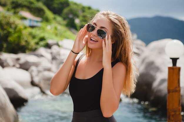 Mulher jovem e elegante hippie sexy de férias, óculos de sol aviador, feliz, sorridente, aproveitando o sol, paisagem de lagoa azul de ilha tropical