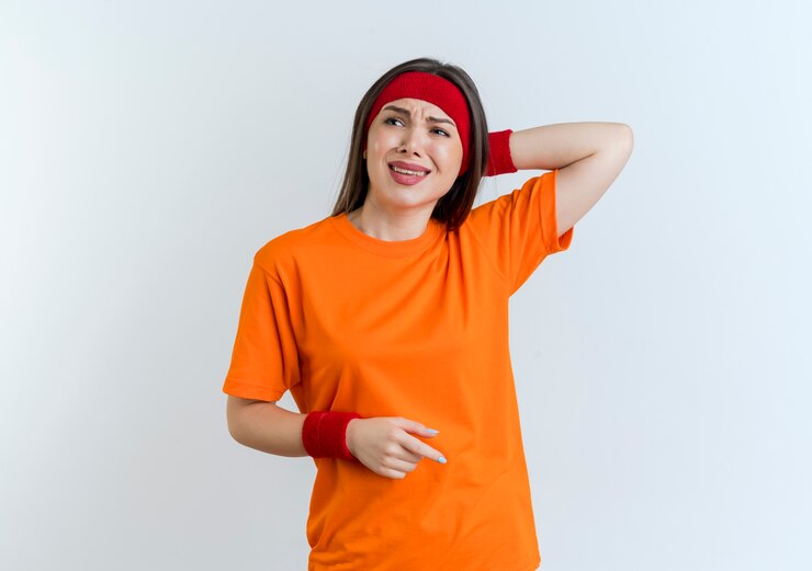 Foto grátis mulher jovem e esportiva irritada usando bandana e pulseiras, mantendo a mão atrás da cabeça, olhando para o lado isolado