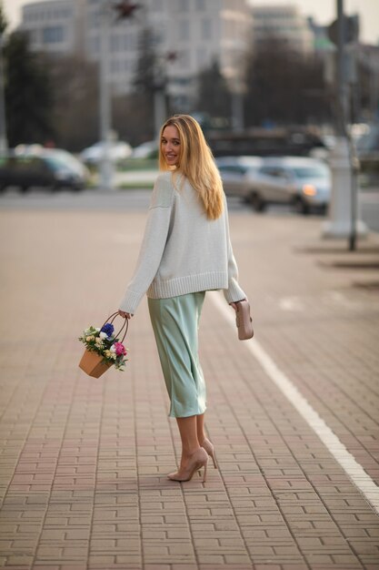 Mulher jovem e feliz, branca, com cabelo longo loiro, caminhando para a rua com um boquet de lindas flores no verão