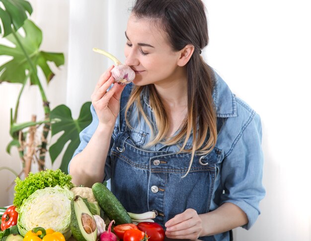 Mulher jovem e feliz comendo salada com vegetais orgânicos na mesa sobre um fundo claro, em roupas jeans. O conceito de comida caseira saudável.