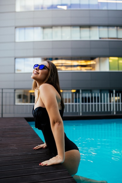 Mulher jovem e linda usa óculos escuros pretos e camiseta preta nadando na piscina no fundo da idade das selvas e relaxa em resort, férias, verão, estilo de vida luxuoso