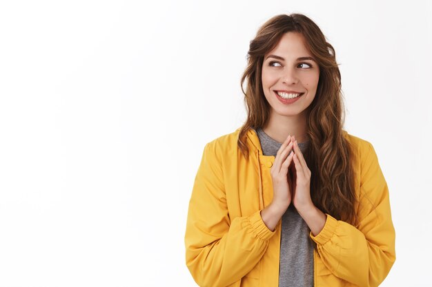 Mulher jovem e misteriosa, criativa e inteligente, girando os dedos pensando excelente ideia, sorrindo, olhando de lado pensando em um esquema tortuoso, pensando em uma parede branca em pé