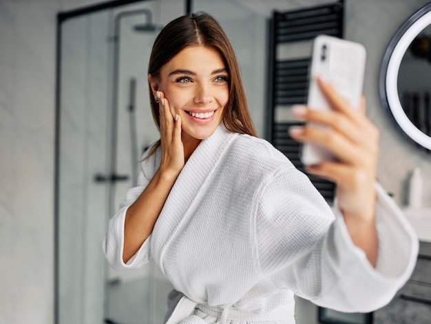 Mulher jovem e positiva em um roupão de banho tirando uma selfie