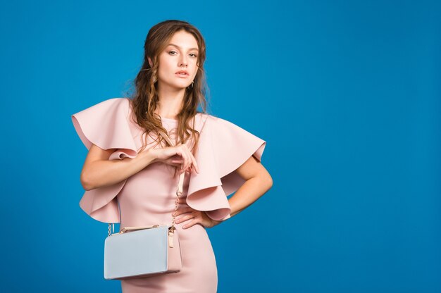 Mulher jovem e sexy elegante em um vestido rosa de luxo, tendência da moda de verão, estilo chique, fundo azul estúdio, segurando uma bolsa da moda