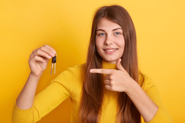 Mulher jovem e sorridente segurando na mão um molho de chaves do carro ou apartamento, apontando para a chave com um sorriso agradável