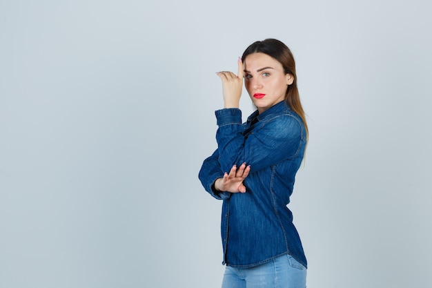 Mulher jovem em camisa jeans e jeans posando em pé e parecendo confiante